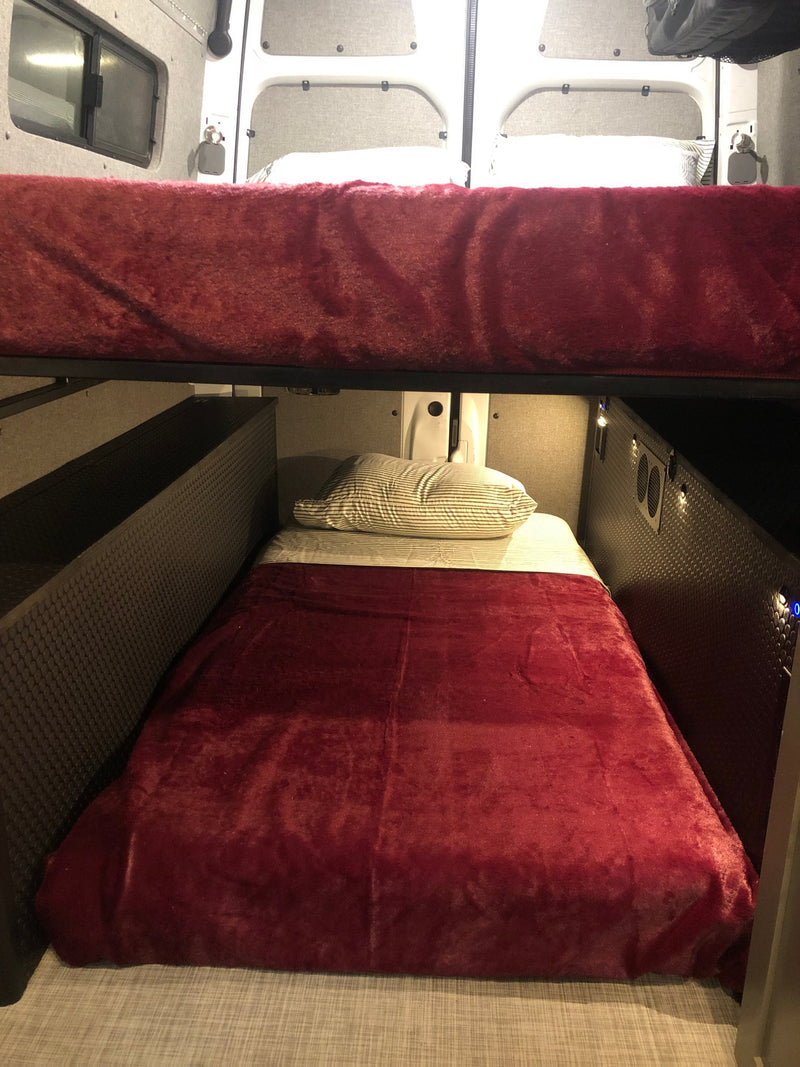 This RV rental features cozy bunk beds. The lower bunk has a striped pillow and red blanket, with textured walls and small lights. — photo 5