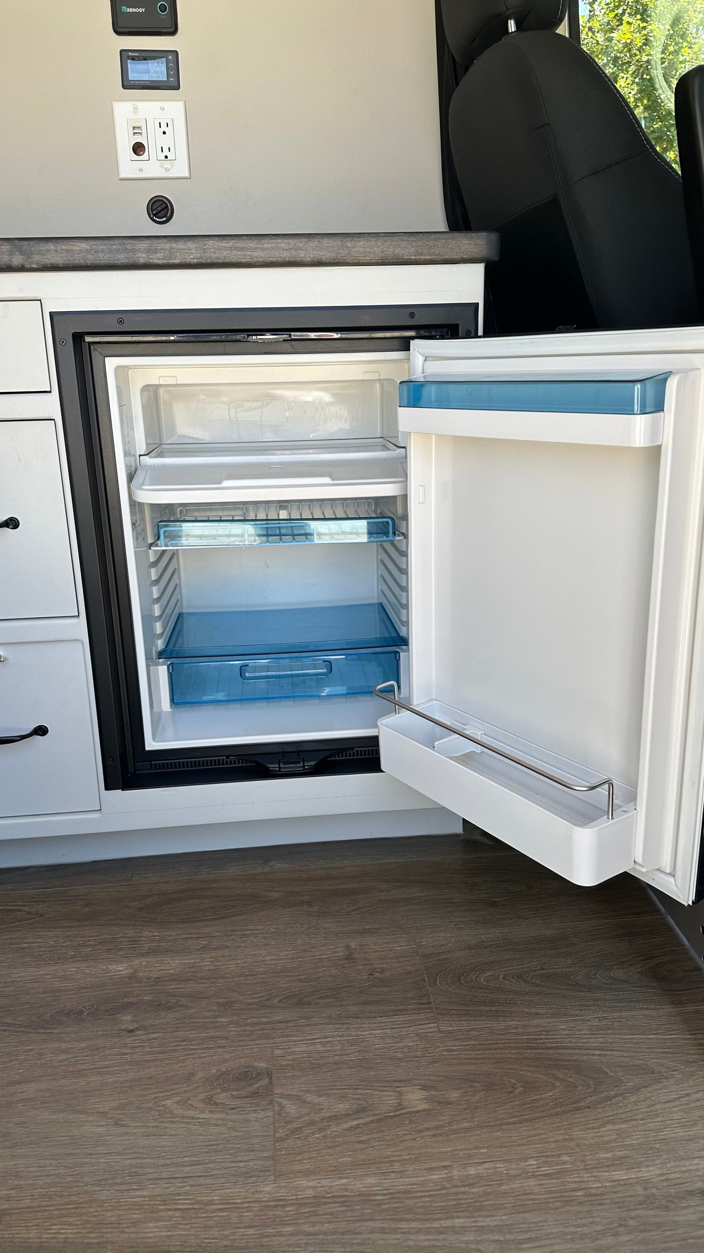 RV rental van interior with open mini-fridge, power outlets, and battery monitor showing 100%.