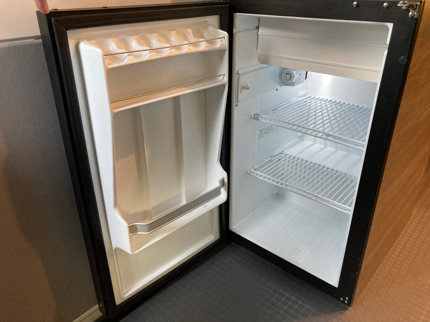 Compact, open refrigerator for an RV rental, with white wire shelves and door storage, perfect for travel essentials.