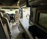 Inside this modern RV rental: compact kitchen with sink, Dometic stovetop, and cozy pet bed. Perfect for travel!