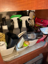 RV rental cleaning essentials: organized under-sink storage with spray bottles, brushes, vacuum, & fire blanket.