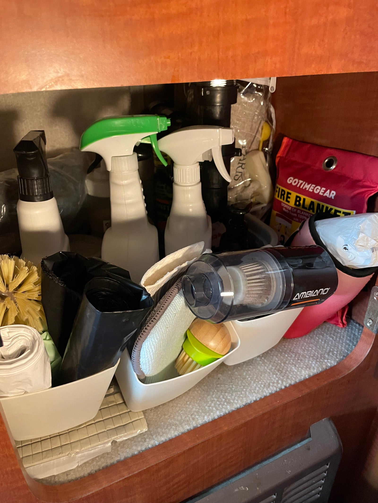 RV rental cleaning essentials: organized under-sink storage with spray bottles, brushes, vacuum, & fire blanket.