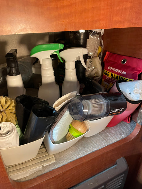 RV rental cleaning essentials: organized under-sink storage with spray bottles, brushes, vacuum, & fire blanket.
