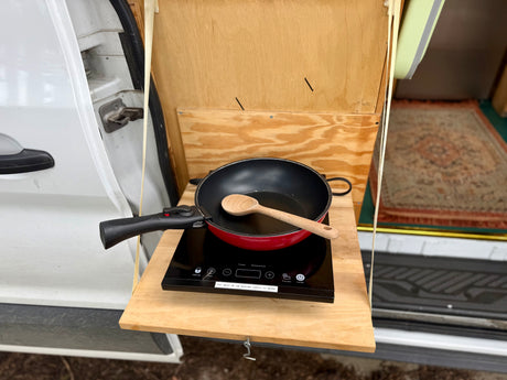RV rental cooking setup: Portable induction cooktop with pan & spoon on a pull-out shelf from a van. Great for camping!