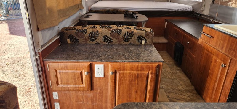 RV rental interior showcasing a dinette, wood cabinetry with power outlet, and kitchen with sink, plus a back bed. — photo 4