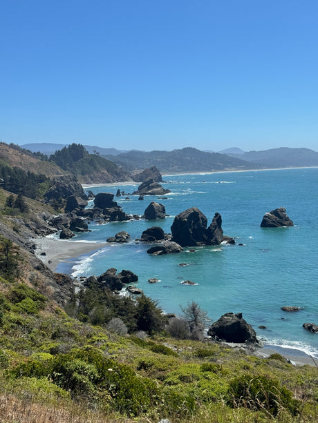 Explore a breathtaking rocky coastline, ideal for an RV rental road trip. Serene blue ocean, sea stacks, and green cliffs.