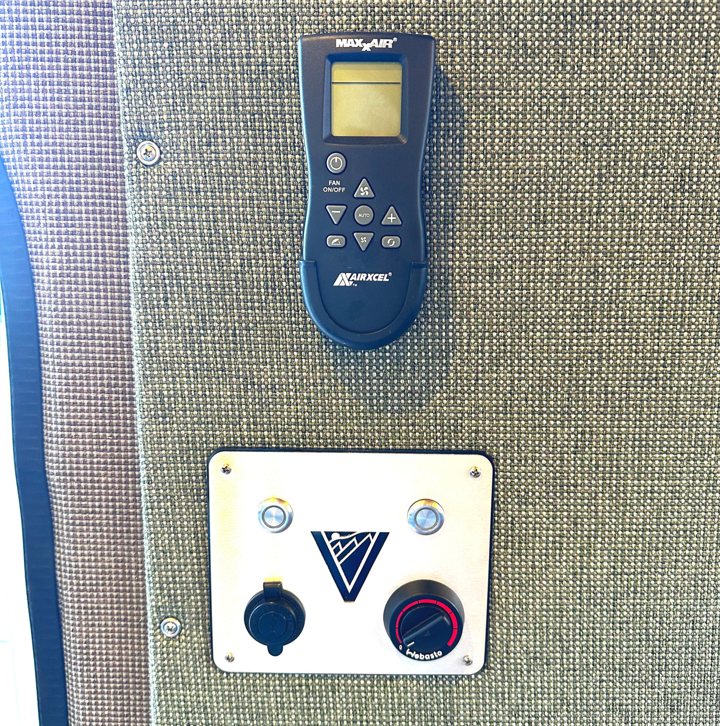 RV rental interior view: MAX X AIR fan remote and Webasto heater controls mounted on a woven fabric wall.