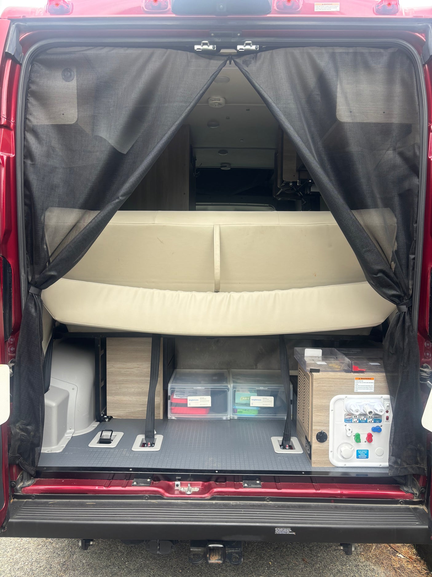 Rear interior of an RV rental with a mesh screen, revealing a bed/bench, storage, and a utility panel on a camper van.