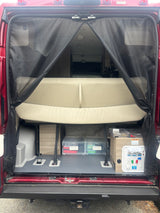 Rear interior of an RV rental with a mesh screen, revealing a bed/bench, storage, and a utility panel on a camper van.
