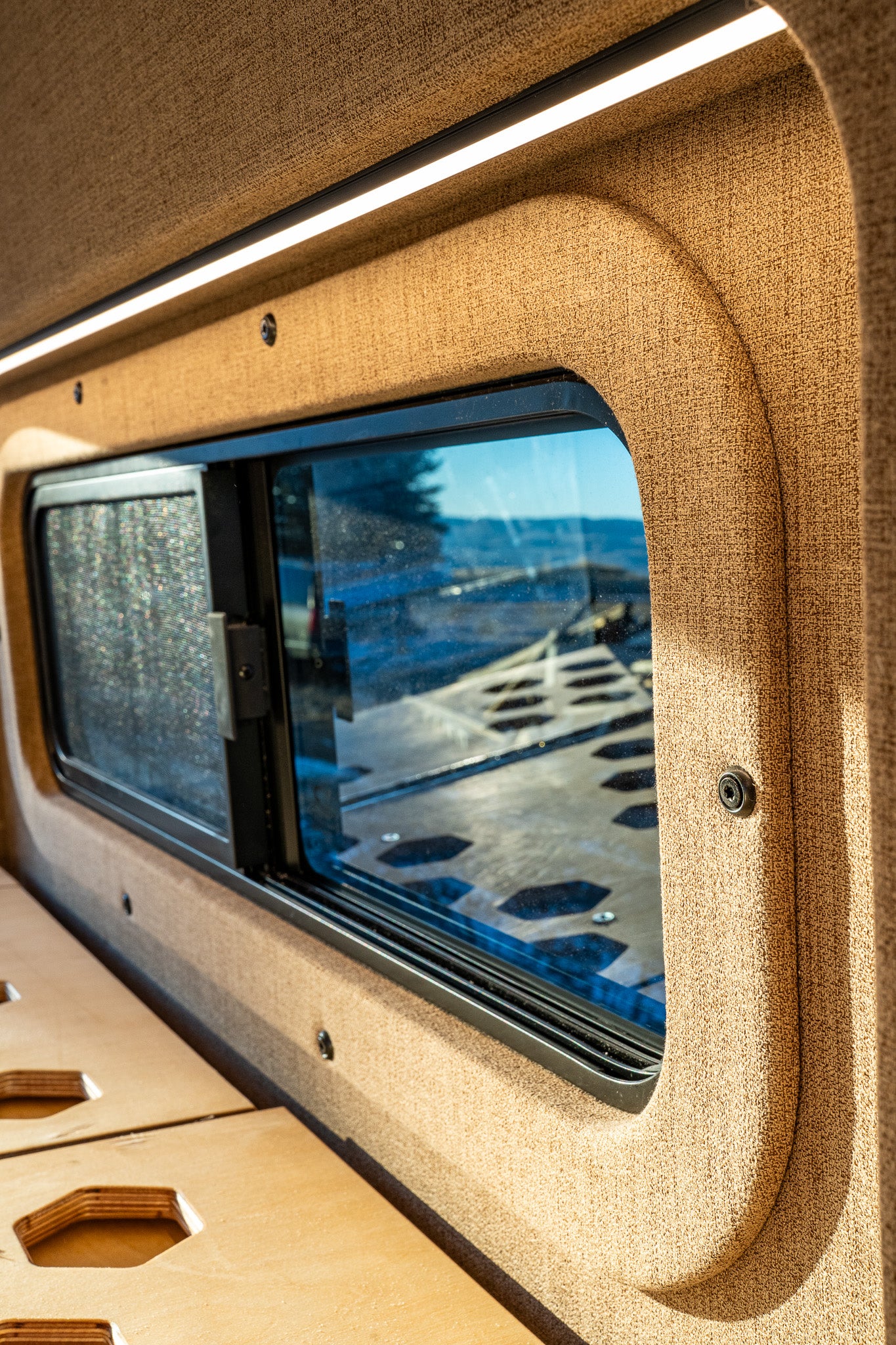 Inside an RV rental: a window offering nature views, sleek LED lighting, and a modular wooden bed platform. Ready for adventure.