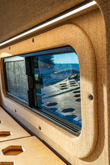 Inside an RV rental: a window offering nature views, sleek LED lighting, and a modular wooden bed platform. Ready for adventure.