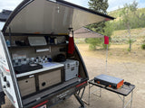 This RV rental's outdoor kitchen features a sink, cooler, and a Blackstone griddle under an awning, perfect for camping.