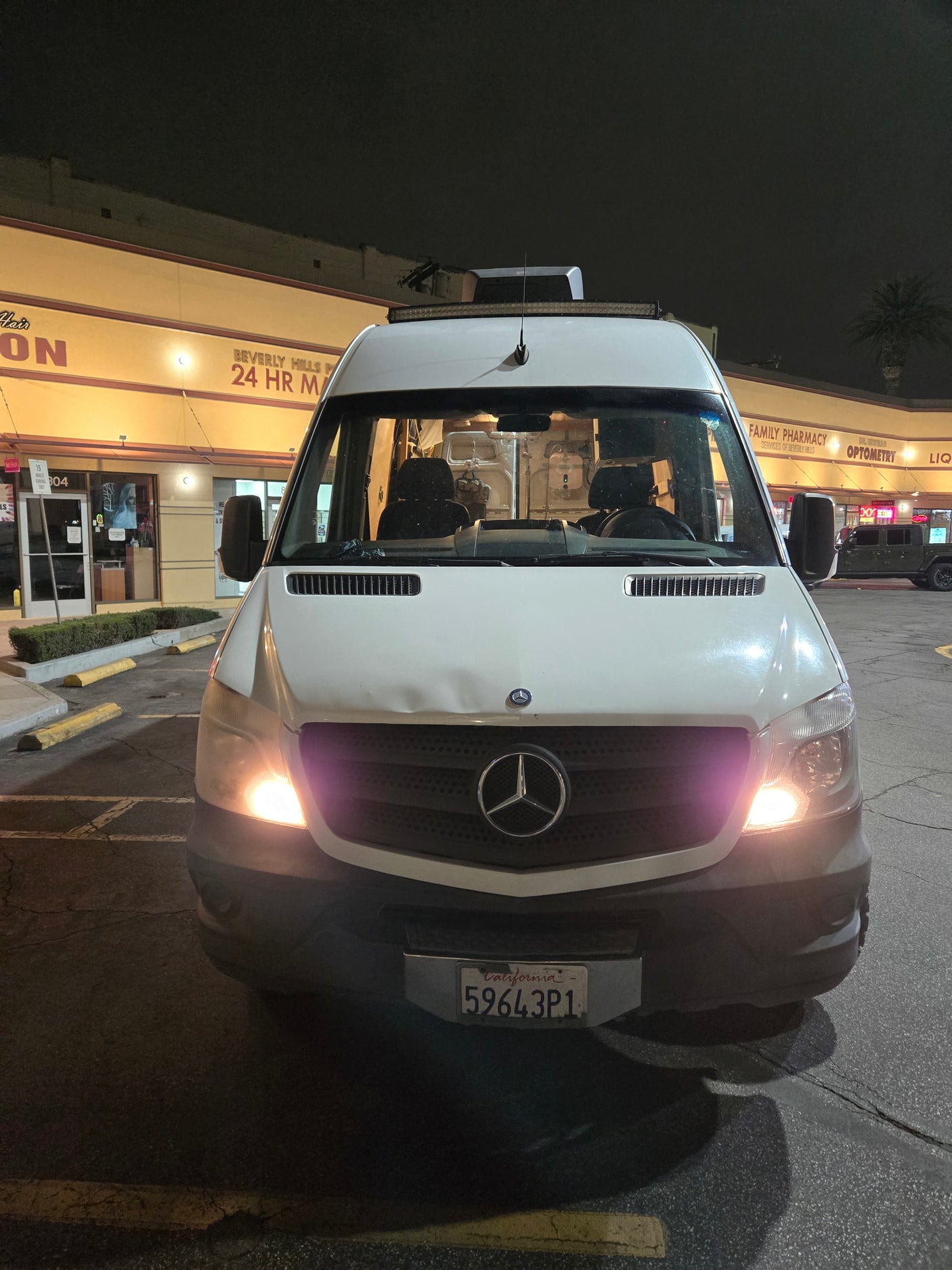 White Mercedes Sprinter van, popular for RV rentals, parked at night outside Beverly Hills shops. CA plate 59643P1.