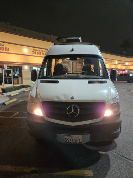 White Mercedes Sprinter van, popular for RV rentals, parked at night outside Beverly Hills shops. CA plate 59643P1.