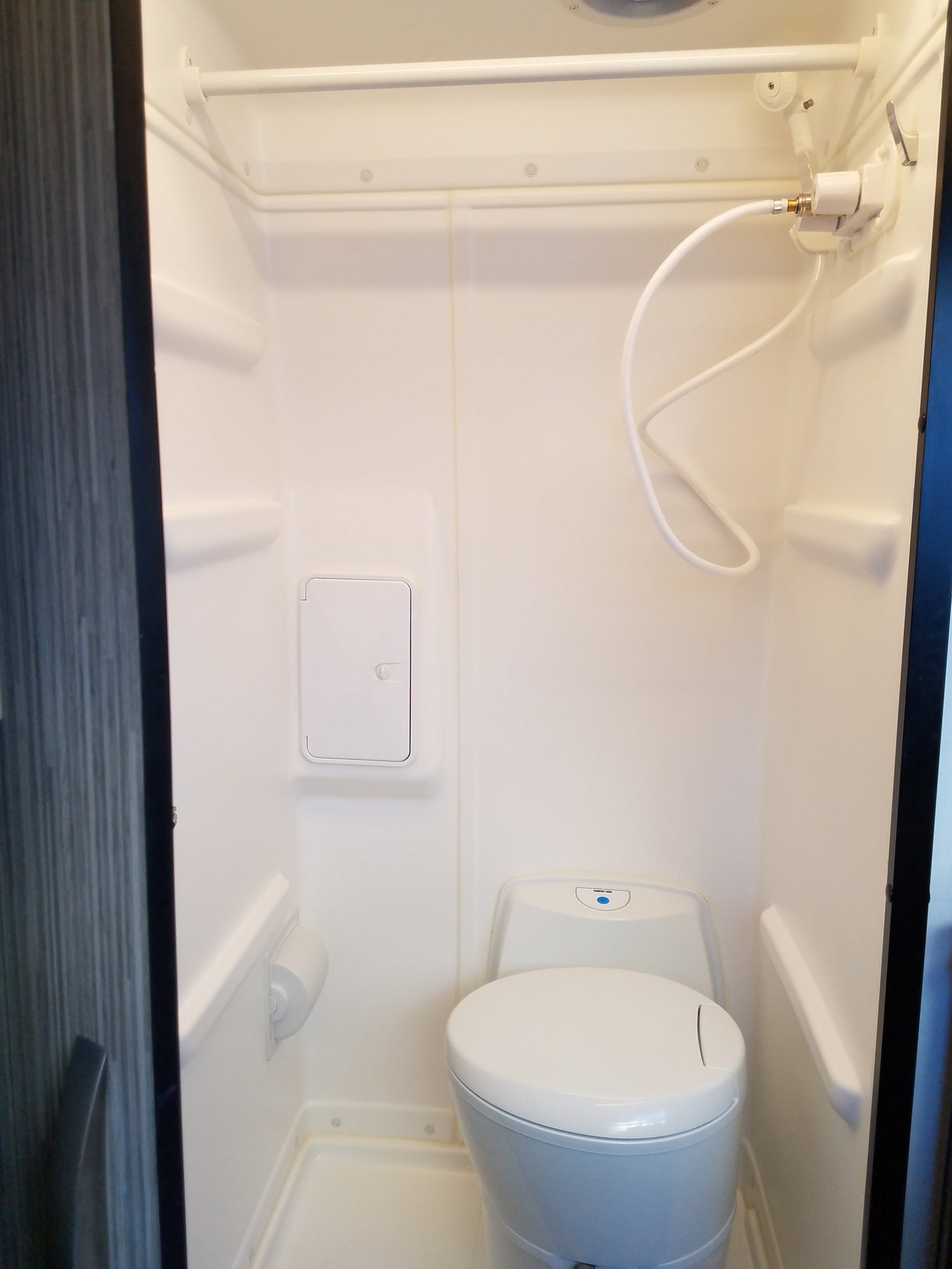 Compact RV rental wet bath featuring a white toilet, hand-held shower, and overhead curtain rod.
