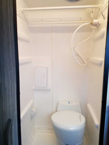 Compact RV rental wet bath featuring a white toilet, hand-held shower, and overhead curtain rod.