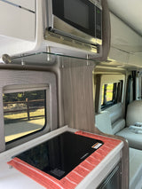 An RV rental interior with a sleek Dometic cooktop, microwave, and light-toned cabinetry, ready for adventure.