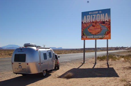 RV rental journey begins! An Airstream trailer next to Arizona's welcome sign on a sunny desert roadside.