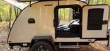 Cozy teardrop camper in a forest, perfect for an RV rental adventure. The side door is open, revealing a comfortable bed.
