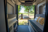 RV rental camper van interior with a mobile office: laptop on wooden table, cozy seating, and a scenic outdoor view.