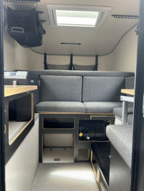 RV rental interior: functional living space with gray upholstered seating, Dometic fridge, and power station.