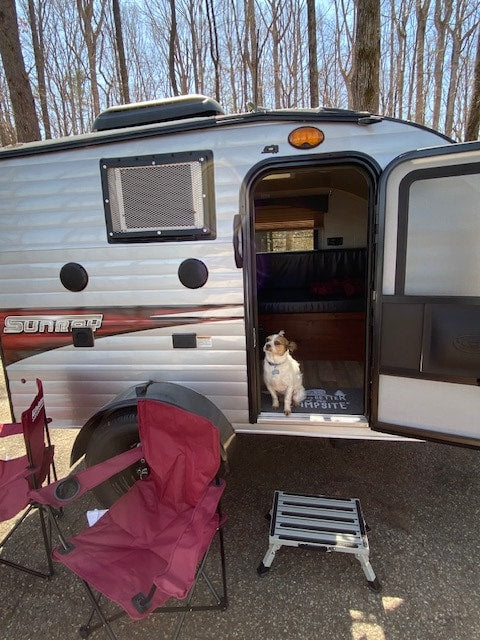  perfect for a peaceful camping getaway.|Sunny day RV rental at a scenic lakeside campsite. A gray travel trailer sits among trees by a blue lake