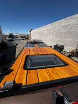 Top-down view of an RV rental roof featuring a wooden deck, skylight, and solar panels for off-grid adventures.