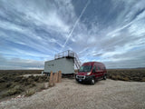 Explore the open landscape! An RV rental is parked next to a unique container home with a rooftop deck under a striking sky.