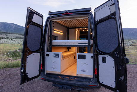 Rear view of a spacious RV rental camper van, showing its custom interior with bunk beds and ambient lighting.