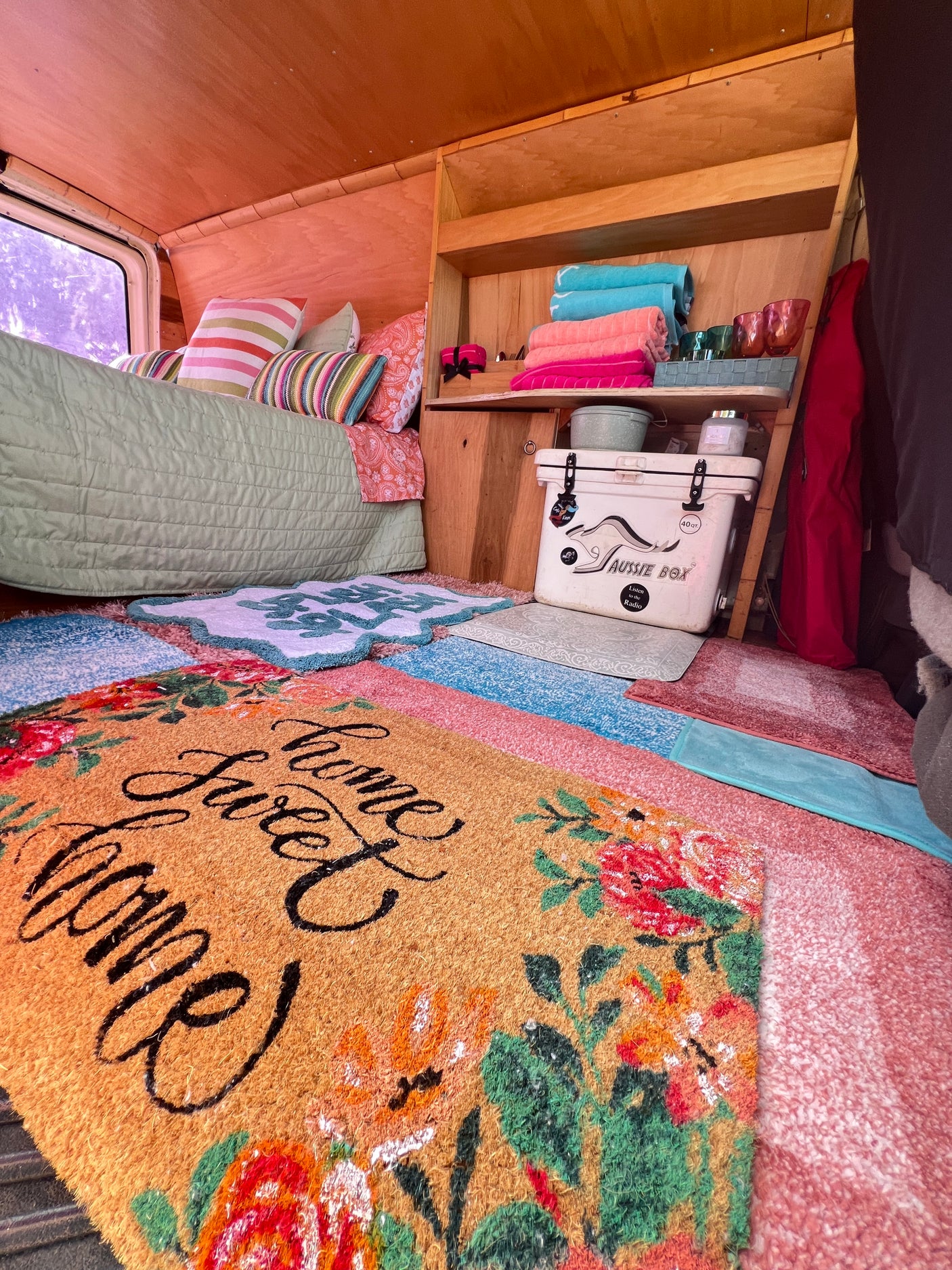 Bright RV rental interior featuring cozy bed, colorful rugs, and smart storage with cooler & towels.