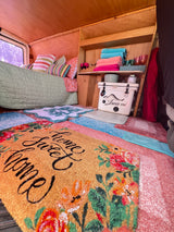 Bright RV rental interior featuring cozy bed, colorful rugs, and smart storage with cooler & towels.