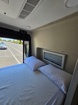 Cozy interior of an RV rental featuring a comfortable bed, window view of the road, and overhead AC unit.