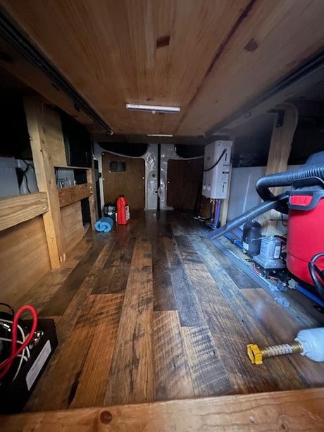 RV rental camper van's under-bed storage, revealing water heater, pump, and electrical systems.