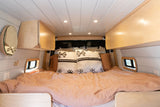 Cozy RV rental bedroom with peach bedding, patterned pillows, light wood cabinets, and small windows for compact living.