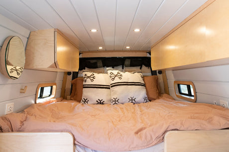 Cozy RV rental bedroom with peach bedding, patterned pillows, light wood cabinets, and small windows for compact living.