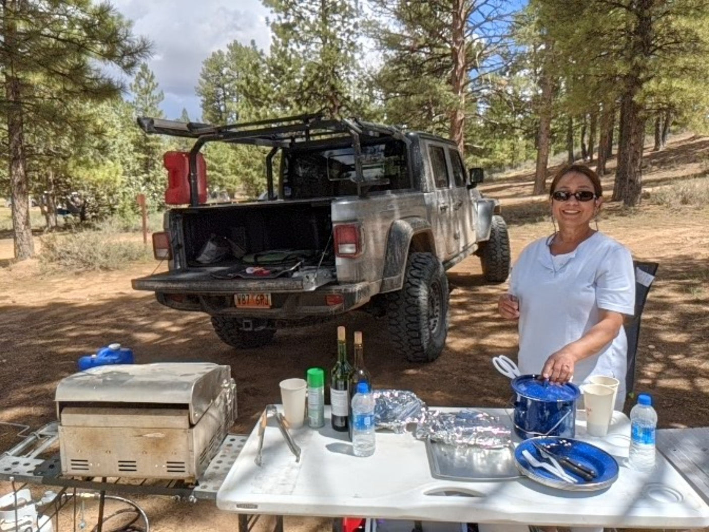 Smiling woman enjoying a campsite meal with a custom Jeep truck, perfect for an RV rental adventure.