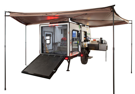 A compact off-road rv rental trailer, with a rear ramp, interior bed, and pull-out outdoor kitchen, under an awning.