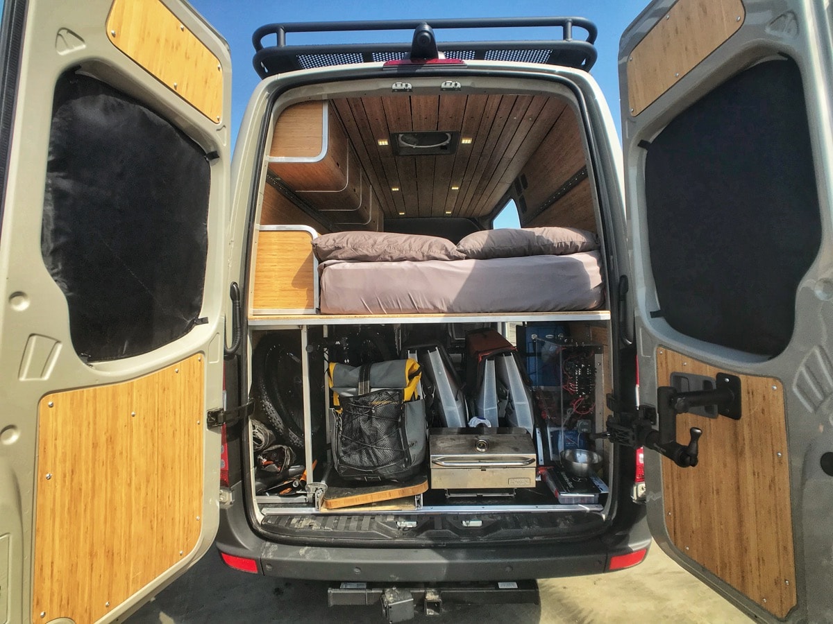 This RV rental showcases a custom camper van's rear: a cozy bed above a spacious gear garage, all with bamboo finishes. — photo 9