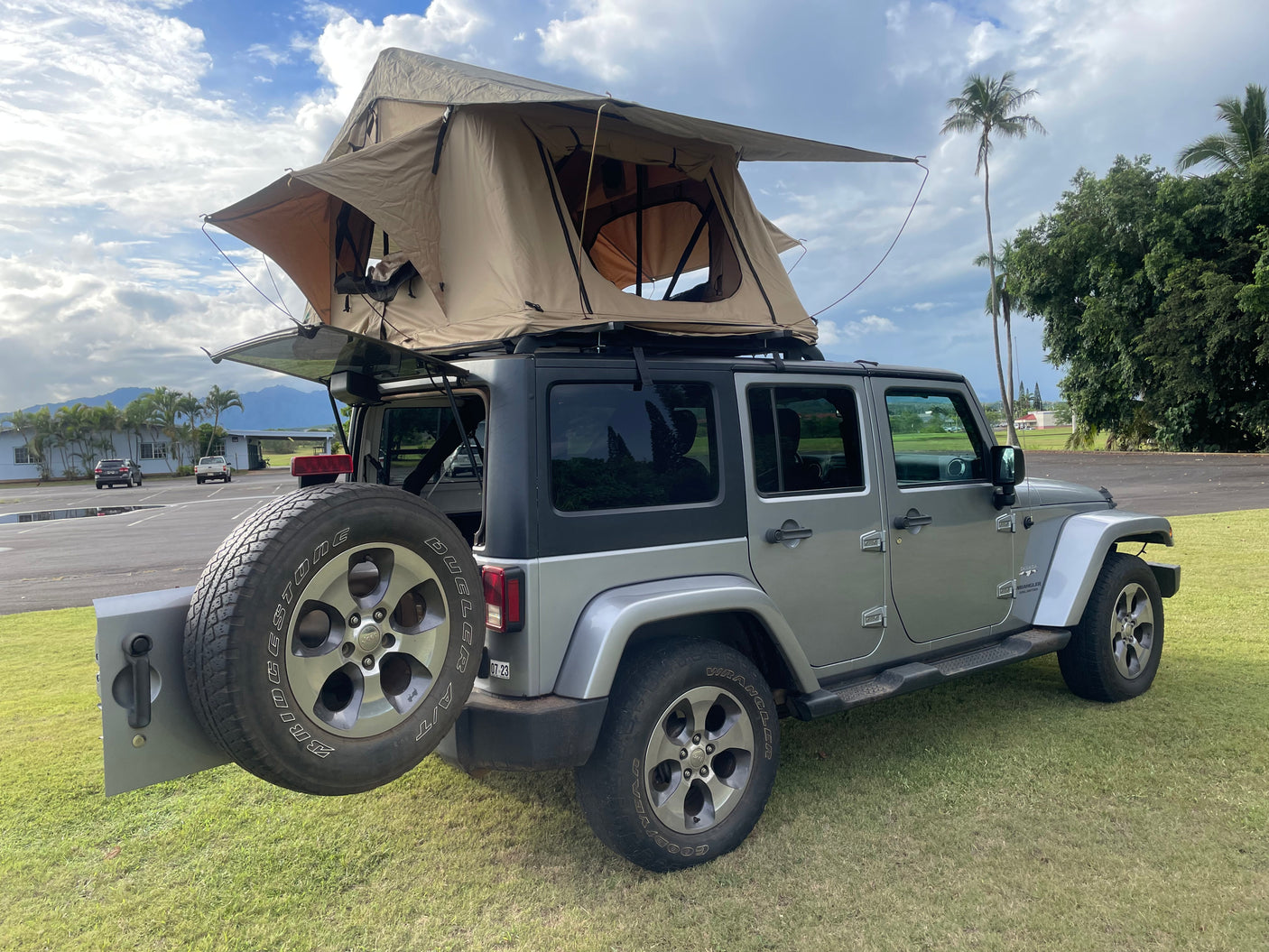This RV rental Jeep Wrangler with an open rooftop tent is ready for your camping and overland adventures, parked on grass near mountains.
