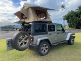 This RV rental Jeep Wrangler with an open rooftop tent is ready for your camping and overland adventures, parked on grass near mountains.
