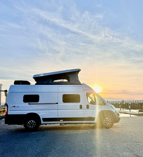 White Winnebago Solis camper van with pop-top open at sunset by a pier, perfect for an RV rental adventure.