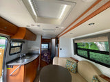 Inside this RV rental: a modern kitchen, comfortable dining/lounge area, and a bed in the rear. Ready for travel.