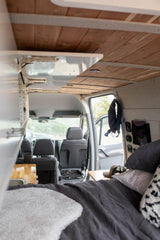 Cozy RV rental interior with a comfy bed, modern wood ceiling, and organized living space, ideal for van life adventures.