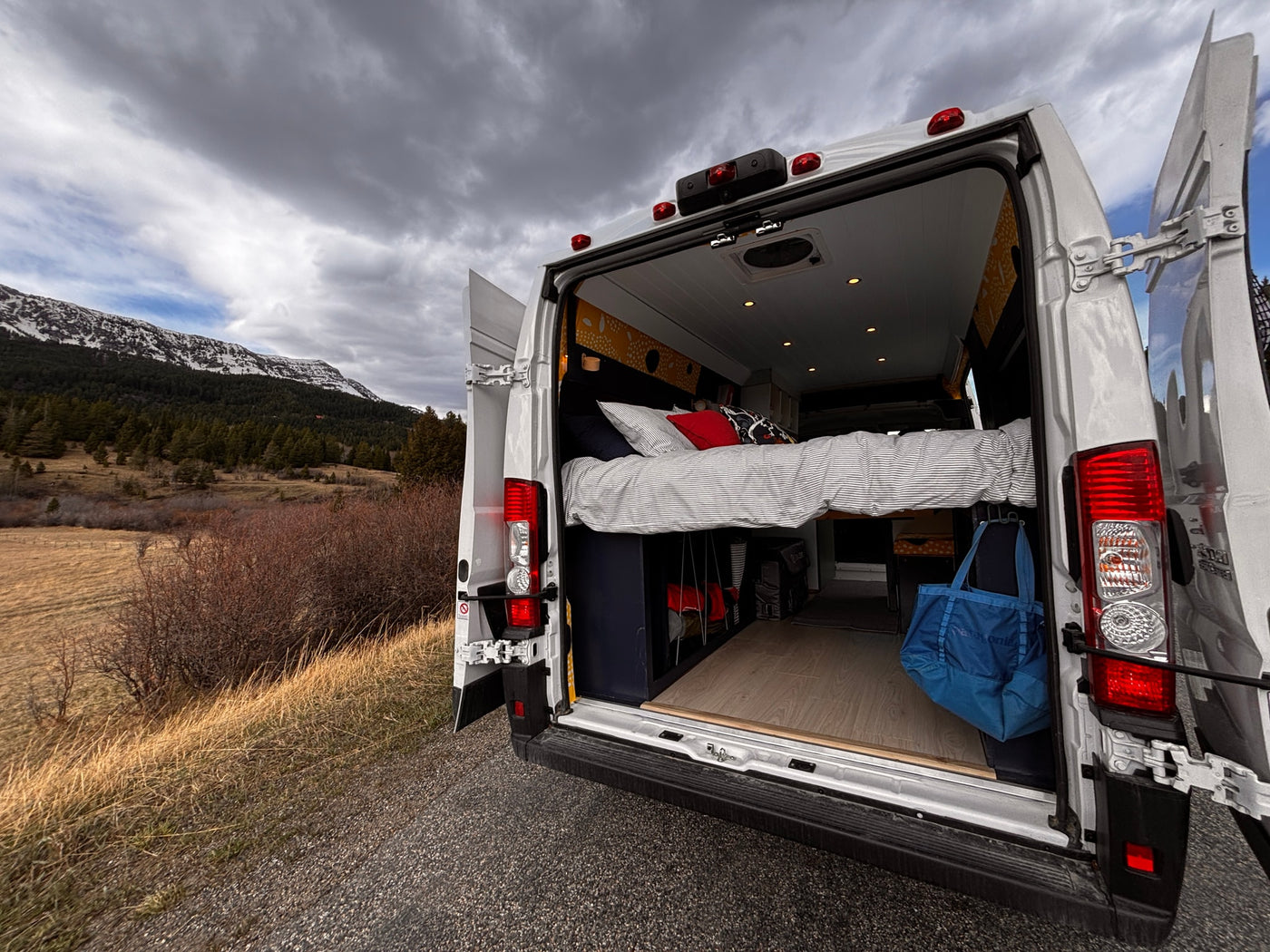 Adventure awaits in this cozy rv rental! Rear doors open to a comfy bed, parked amidst mountains & cloudy skies. — photo 19