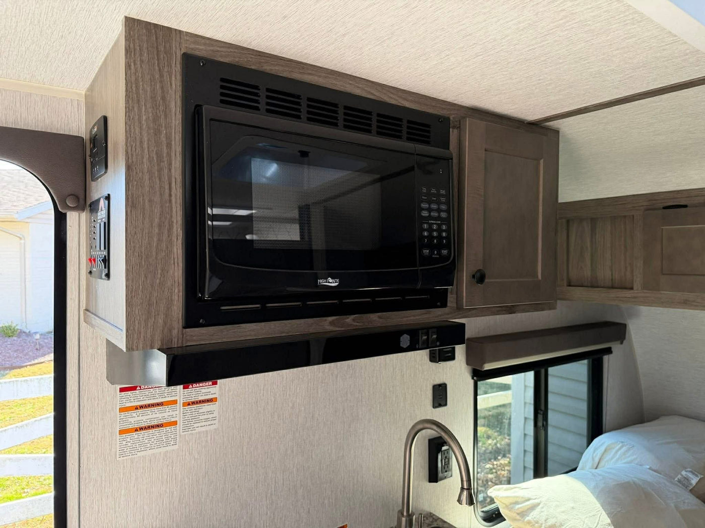 RV rental interior: Compact kitchen with overhead microwave, sink, and adjacent sleeping area for travel comfort. — photo 12