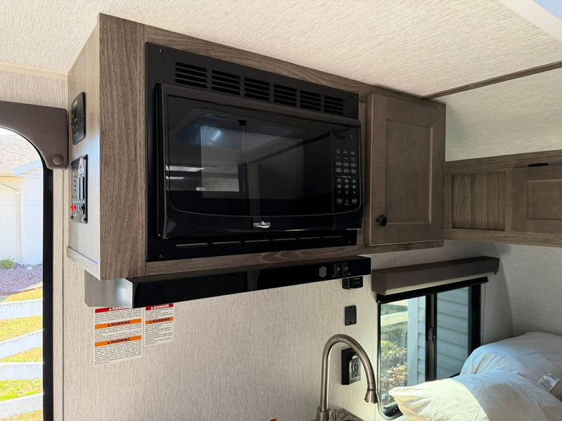 RV rental interior: Compact kitchen with overhead microwave, sink, and adjacent sleeping area for travel comfort. — photo 12