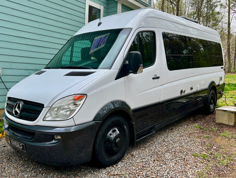 Two-tone white & black Mercedes-Benz Sprinter camper van, an ideal rv rental, parked on gravel next to a light blue house.