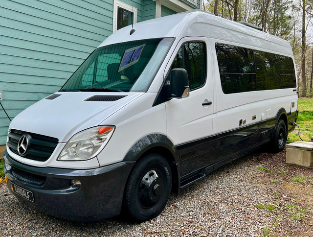 Two-tone white & black Mercedes-Benz Sprinter camper van, an ideal rv rental, parked on gravel next to a light blue house.