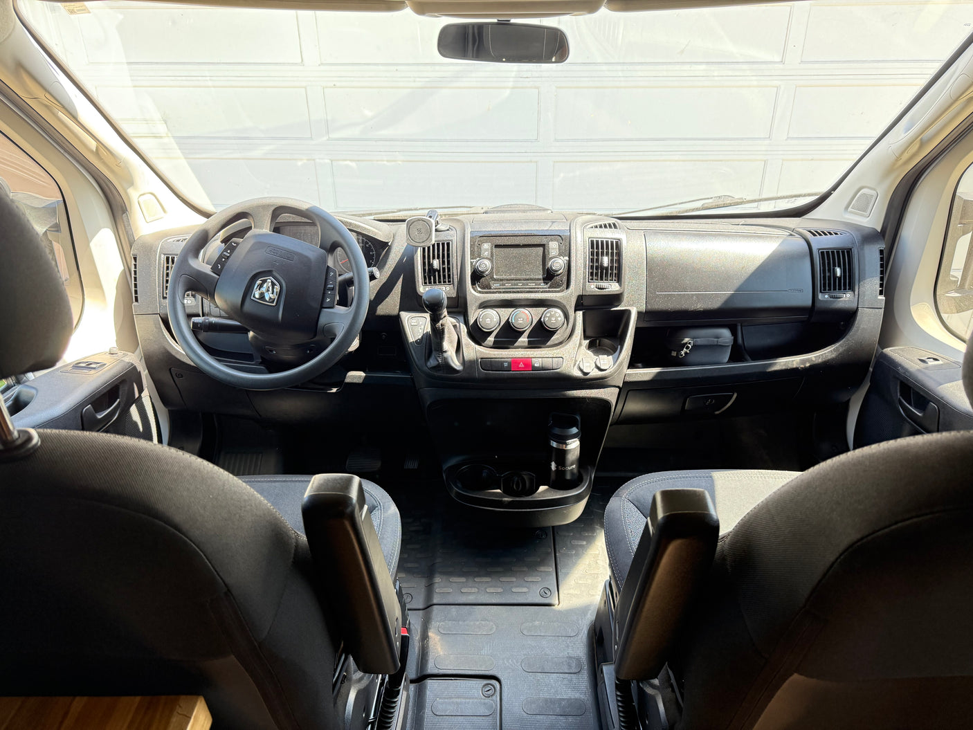 RV rental van's front cabin. View from rear seats showing steering wheel, dashboard controls, and spacious interior.