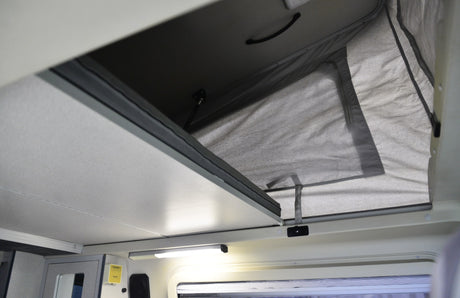 Inside an RV rental, showing the elevated pop-top bed and fabric tent walls, providing extra sleeping space.